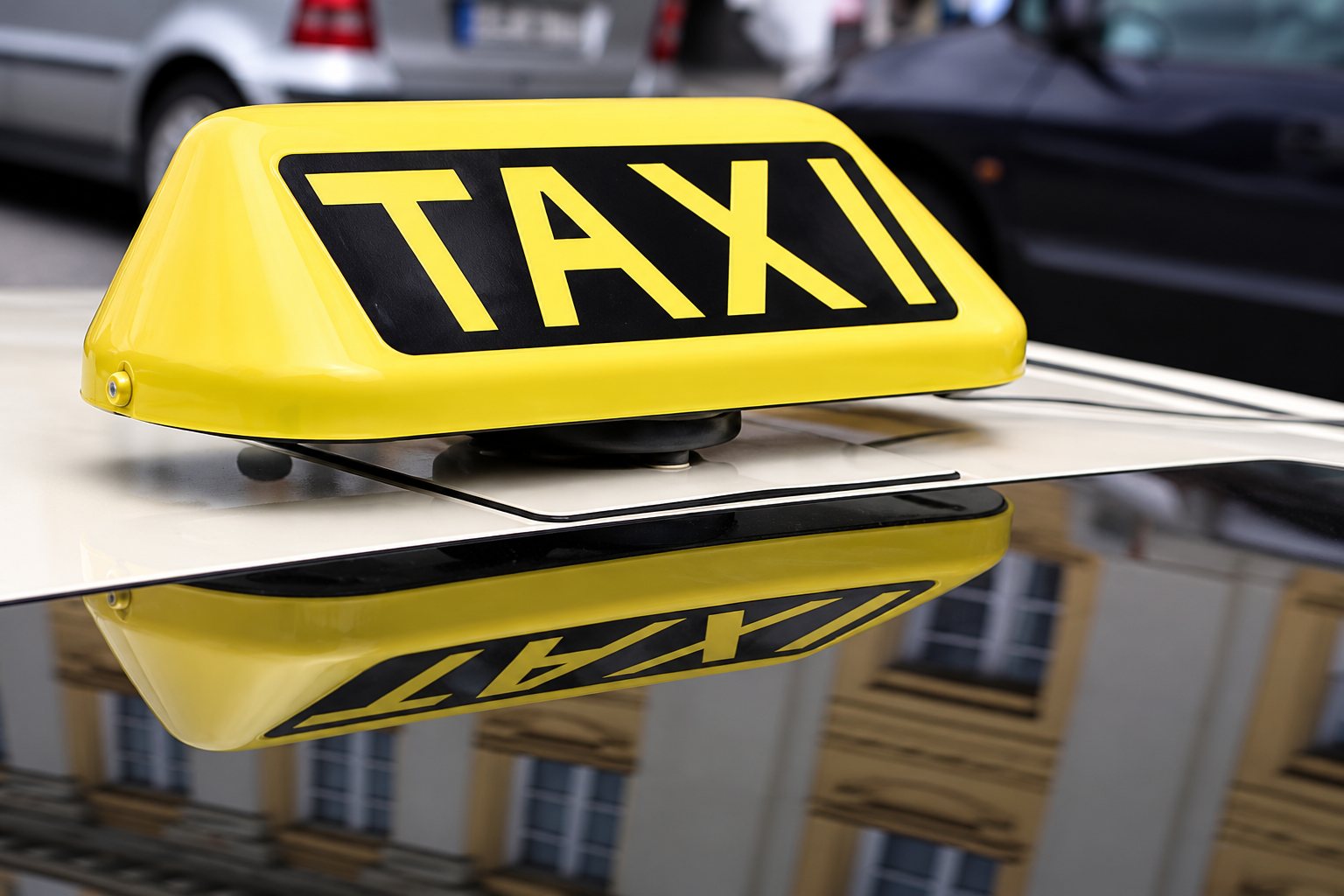 Gros plan sur un panneau lumineux jaune portant l'inscription TAXI en noir, fixé sur le toit d'un véhicule.