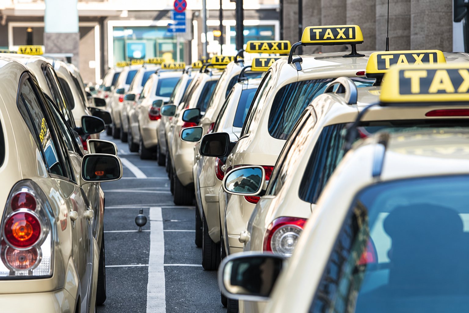 Une longue file de taxis beiges avec leurs enseignes lumineuses jaunes TAXI garés côte à côte dans une station.