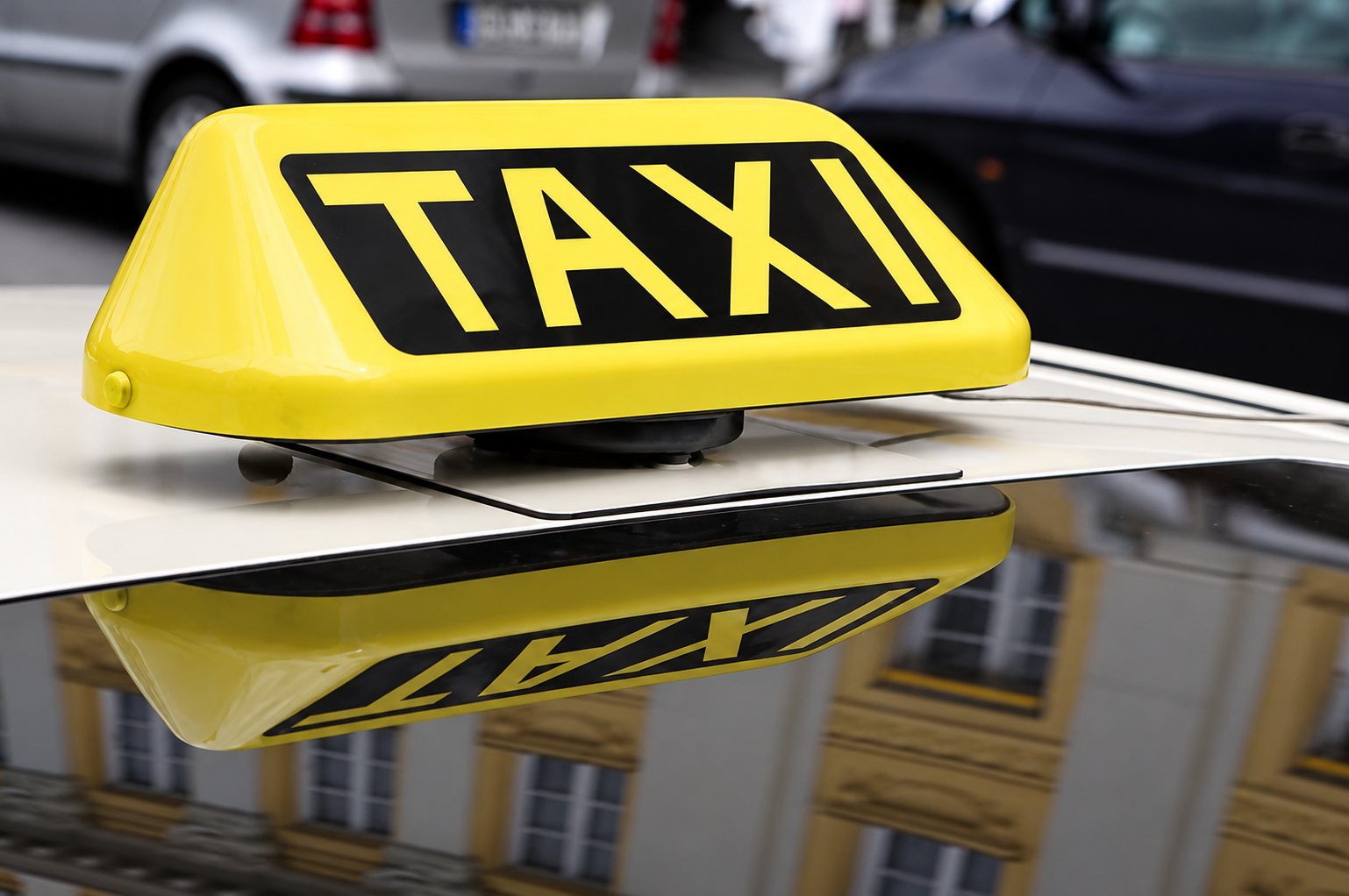 Gros plan sur un panneau lumineux jaune portant l'inscription TAXI, posé sur le toit d'une voiture blanche.