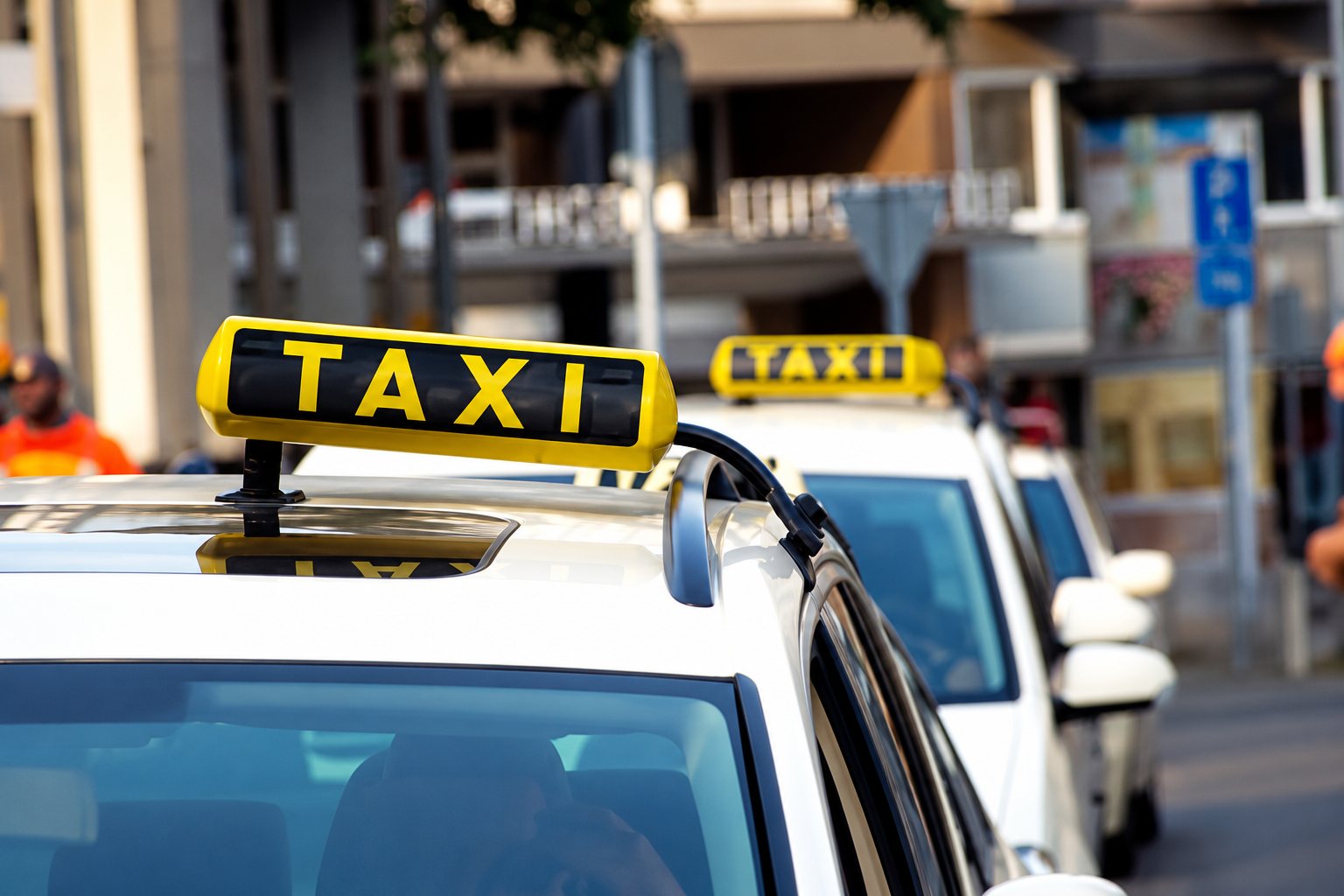 Plusieurs taxis blancs surmontés d'enseignes jaunes portant l'inscription TAXI, stationnés dans une rue de ville.